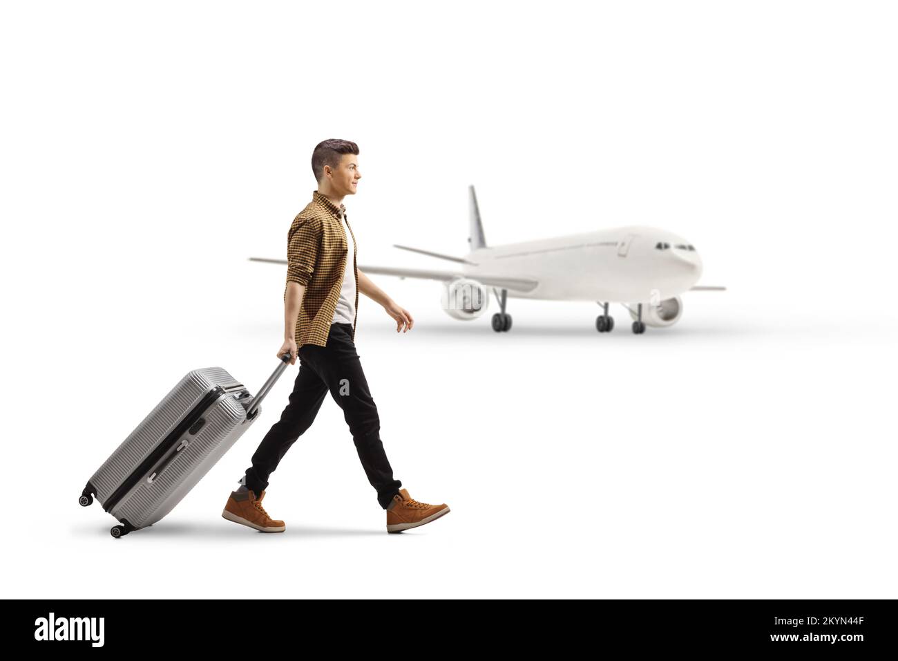 Vue en profil d'un jeune homme marchant et tirant une valise devant un avion isolé sur fond blanc Banque D'Images