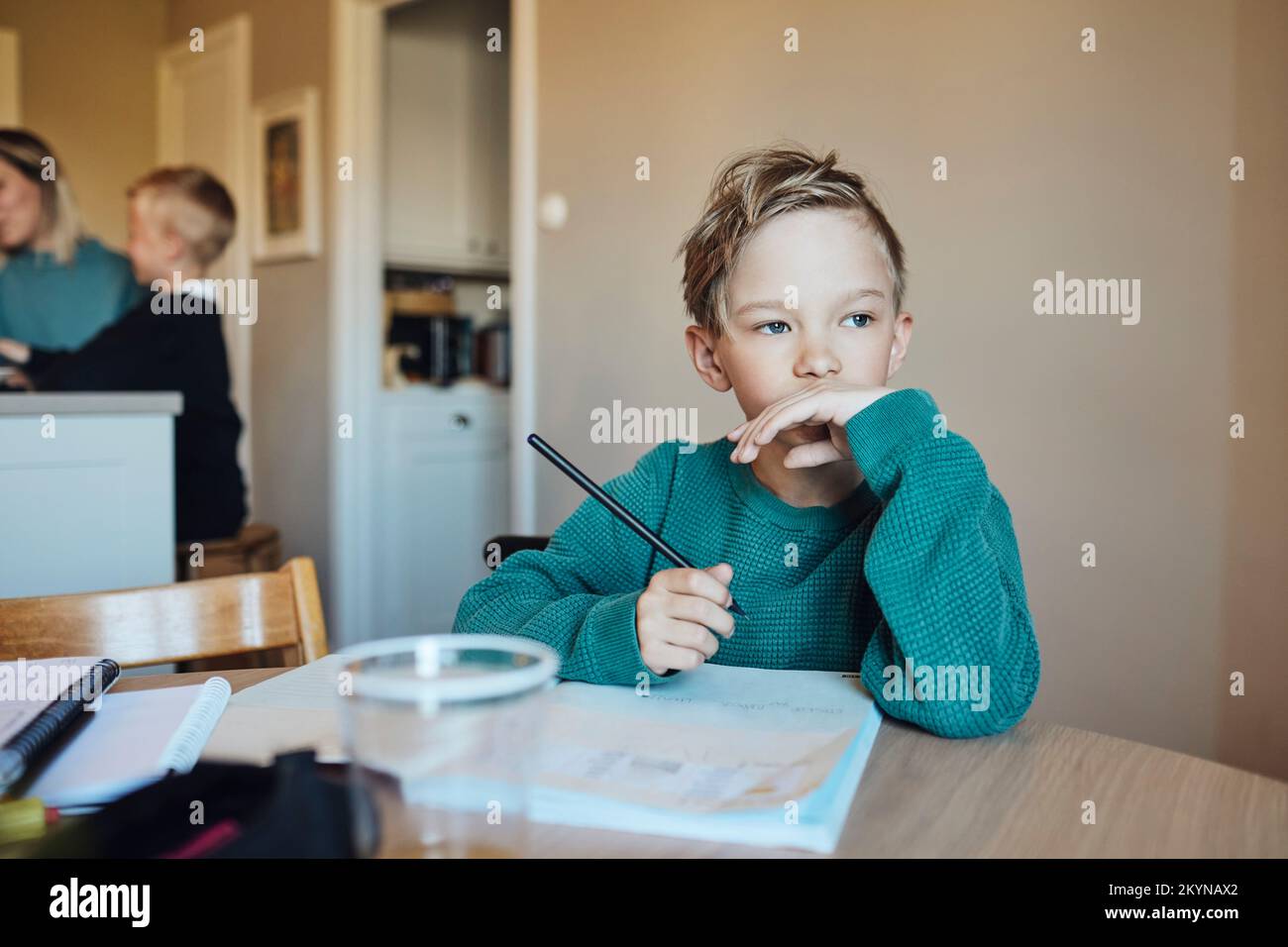 Un garçon attentionné avec un crayon et un livre assis à table Banque D'Images