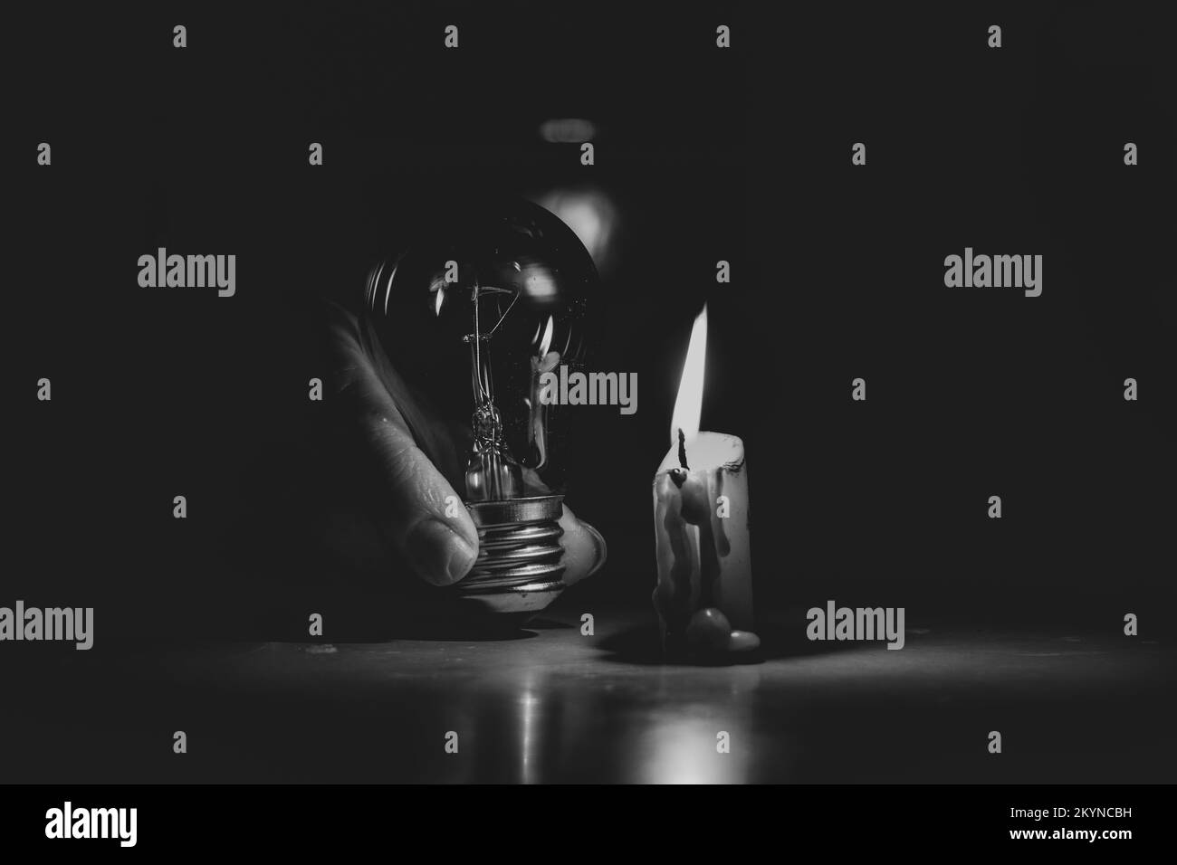 La main d'une femme tient une ampoule près d'une bougie sur une table à la maison en Ukraine, pas de lumière, des gens sans lumière, sombre Banque D'Images