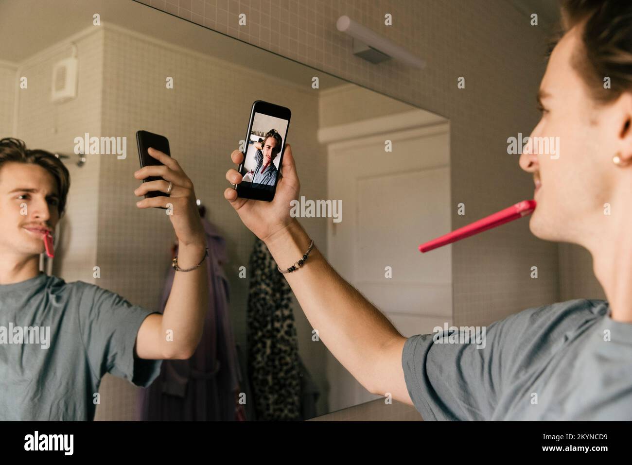 Homme se brossant les dents prenant selfie par téléphone portable dans la salle de bains à la maison Banque D'Images