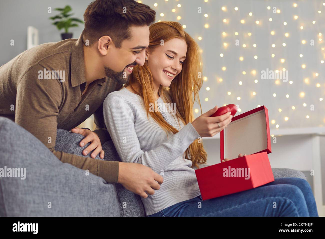 Femme souriante assise et sortant les coeurs rouges de la boîte cadeau de son petit ami Banque D'Images