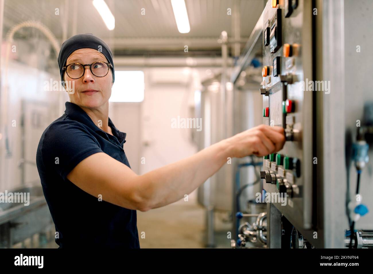 Une agricultrice portant des lunettes faisant fonctionner la machine à l'usine laitière Banque D'Images