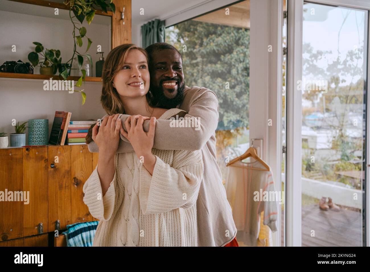 Portrait d'un homme souriant qui embrasse sa petite amie tout en restant debout à la maison Banque D'Images