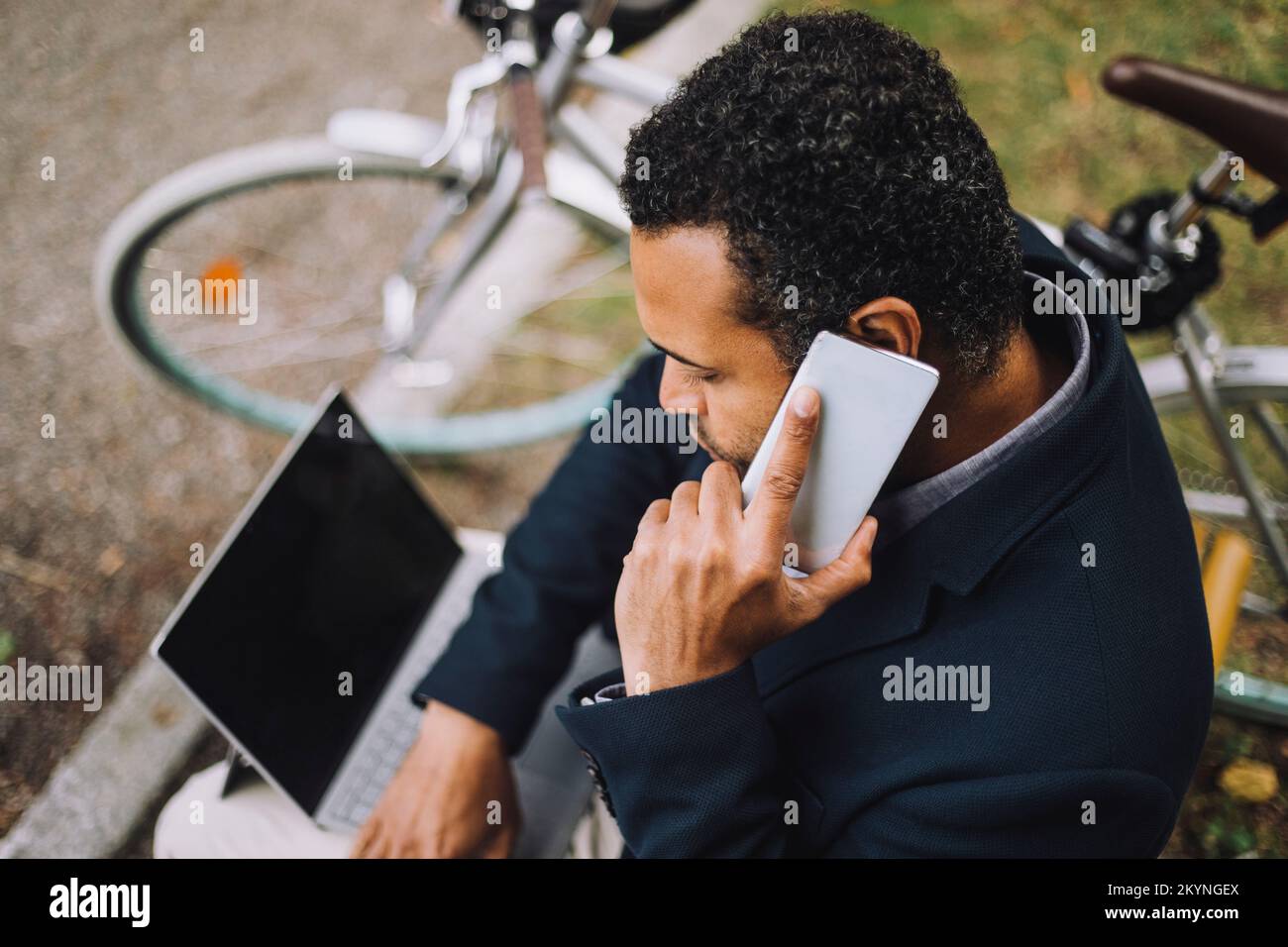 Vue en grand angle d'un homme d'affaires parlant sur un smartphone tout en étant assis avec un ordinateur portable dans le parc Banque D'Images