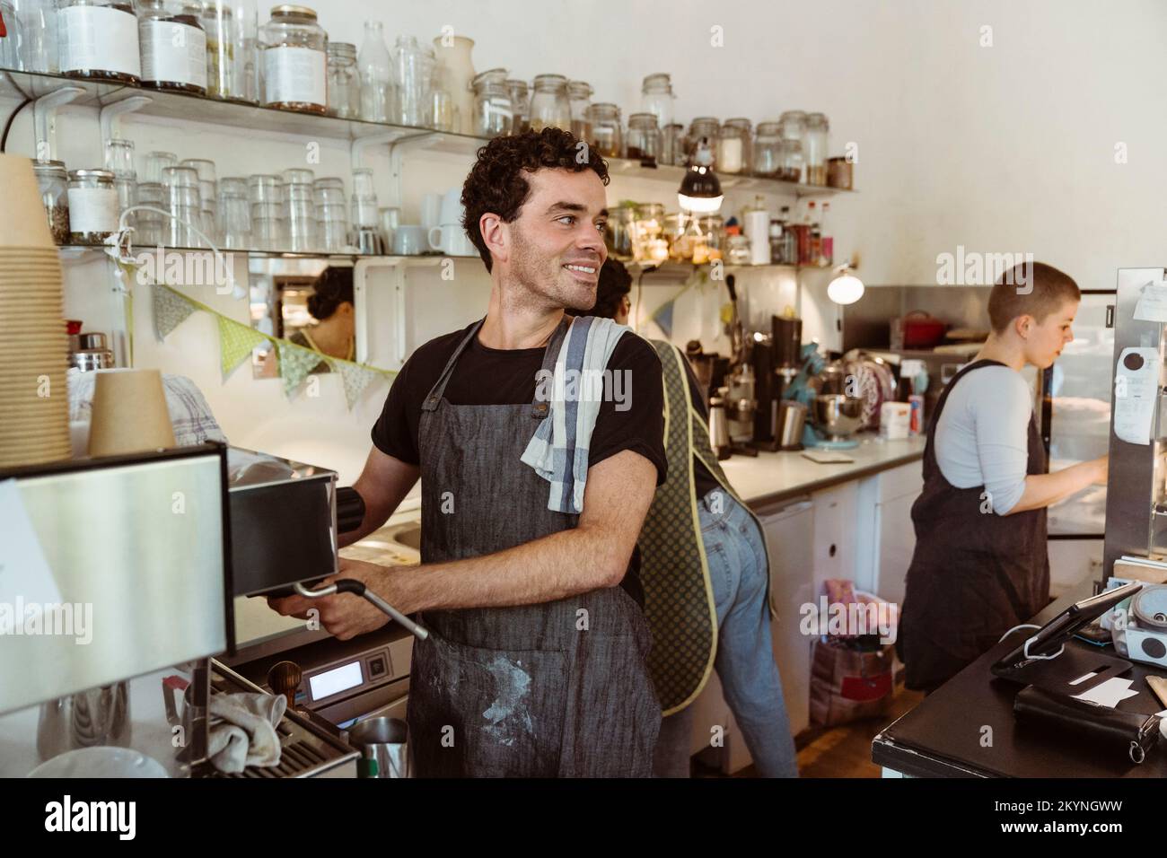 Le propriétaire souriant a vue sur l'extérieur tout en préparant un café au café Banque D'Images