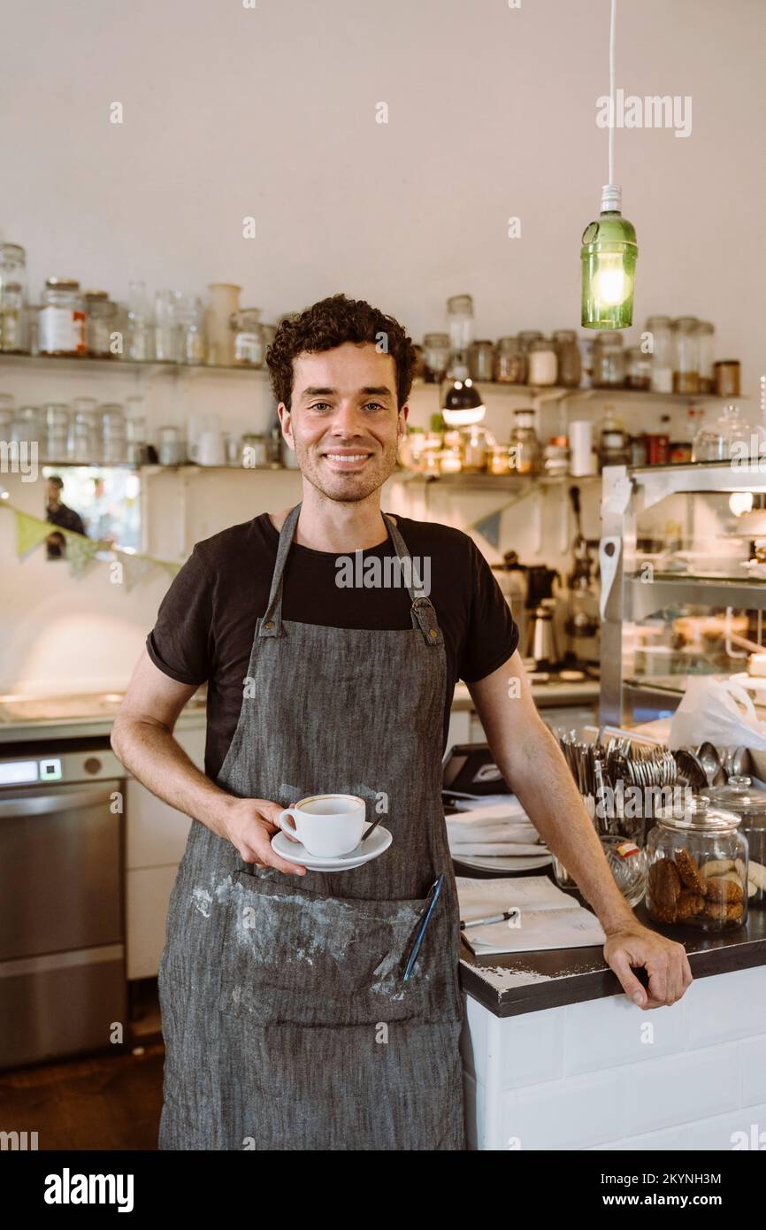 Un homme souriant tenant une tasse de café debout dans un café Banque D'Images