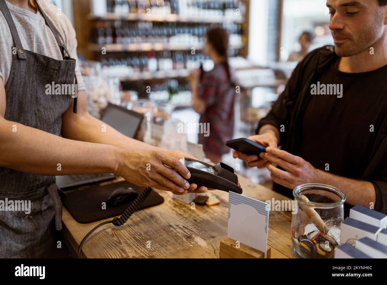 Section intermédiaire du propriétaire masculin donnant la machine de carte de crédit au client faisant le paiement en ligne au magasin Banque D'Images