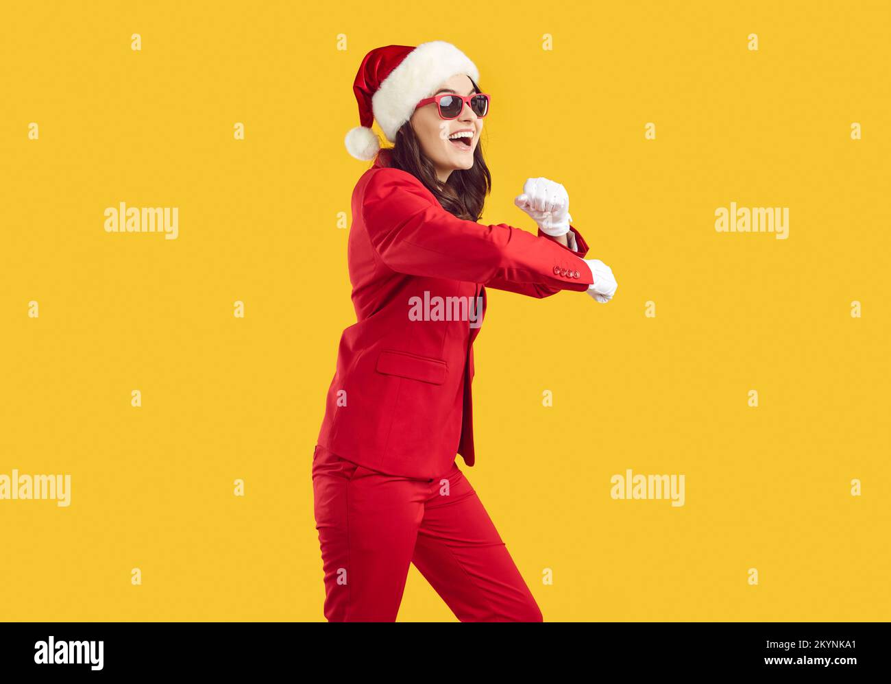 Jeune femme joyeuse en costume rouge, lunettes de soleil et chapeau de Noël dansant sur fond jaune Banque D'Images