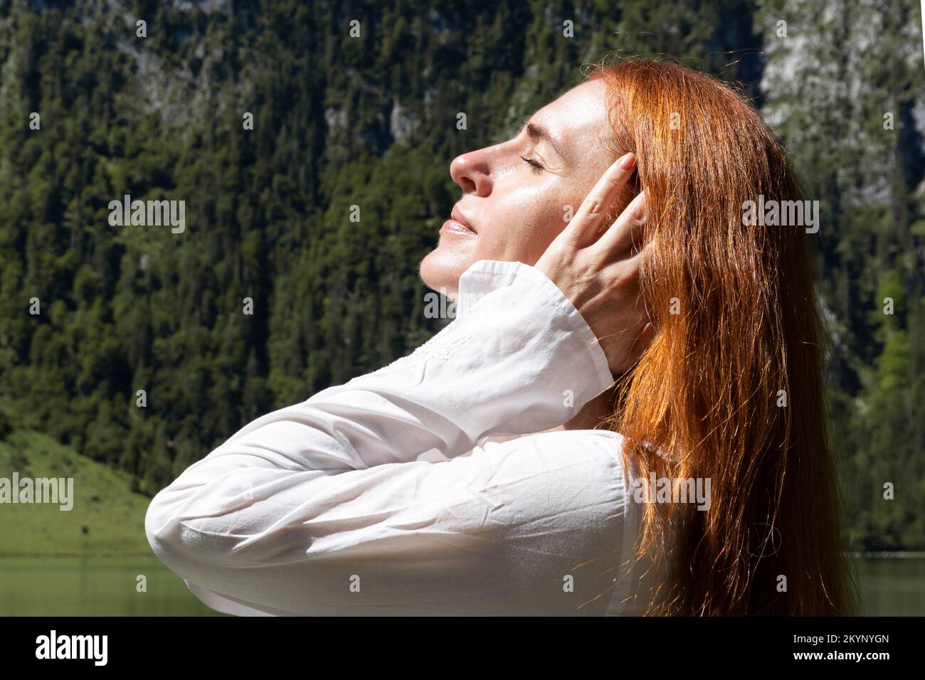 Une belle femme aux cheveux rouges avec ses yeux fermés bénéficie d'une chaude journée d'été et d'un bon temps. Banque D'Images