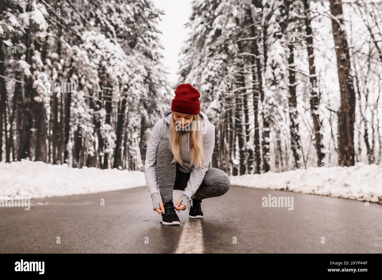 Jeune femme sportive qui s'échauffe avant son entraînement d'hiver pendant une journée ensoleillée et enneigée Banque D'Images