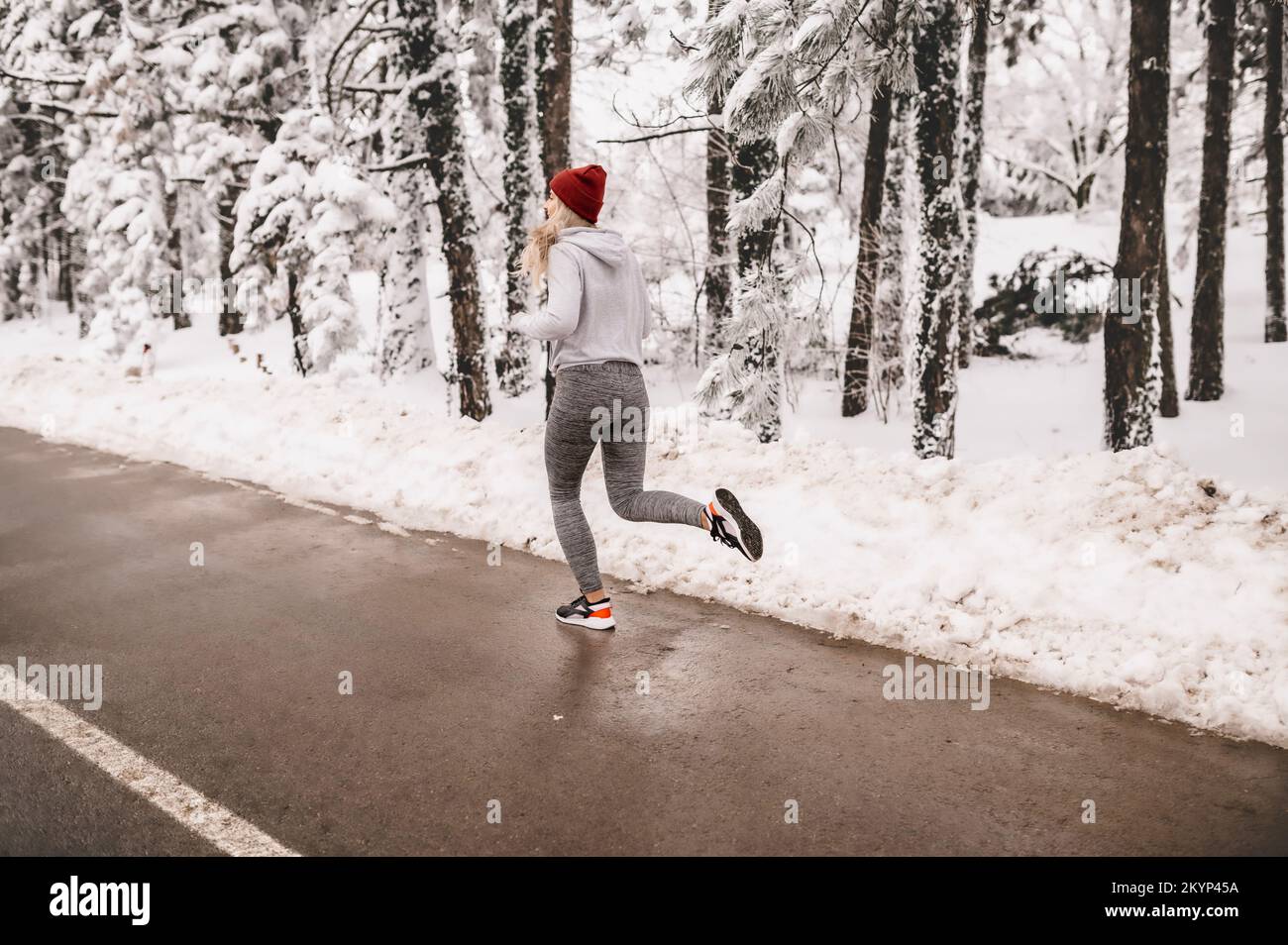 Jeune femme sportive qui s'échauffe avant son entraînement d'hiver pendant une journée ensoleillée et enneigée Banque D'Images