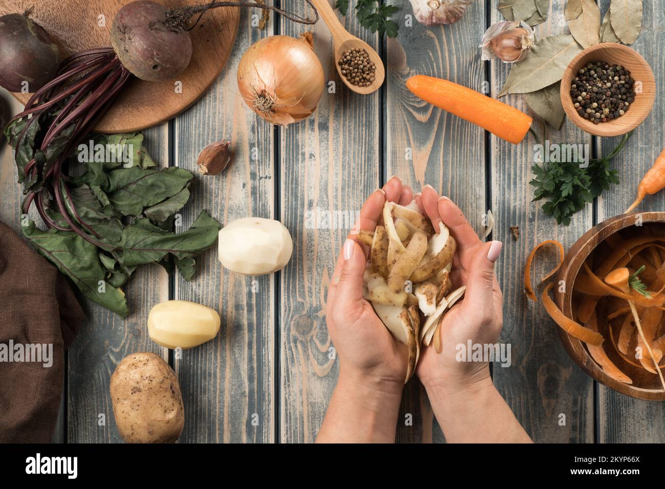 Les mains humaines tiennent une poignée de pelures de pommes de terre pelées, étassées. Mélange de légumes biologiques frais crus sur une table en bois. Aliments sains, ingrédients pour la cuisson. Banque D'Images