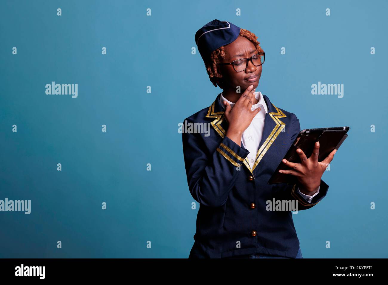 L'hôtesse afro-américaine porte l'uniforme de la compagnie aérienne en regardant attentivement l'écran des tablettes numériques. Une femme qui vérifie le nouvel horaire de travail semble confuse avec les changements. Banque D'Images