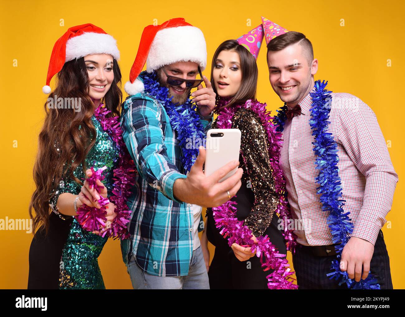 Groupe ou compagnie d'amis dans le chapeau de santa, chapeaux de fête, boas célébrant Noël, s'amuser, prendre des selfies et de vivre sur un fond jaune. Banque D'Images