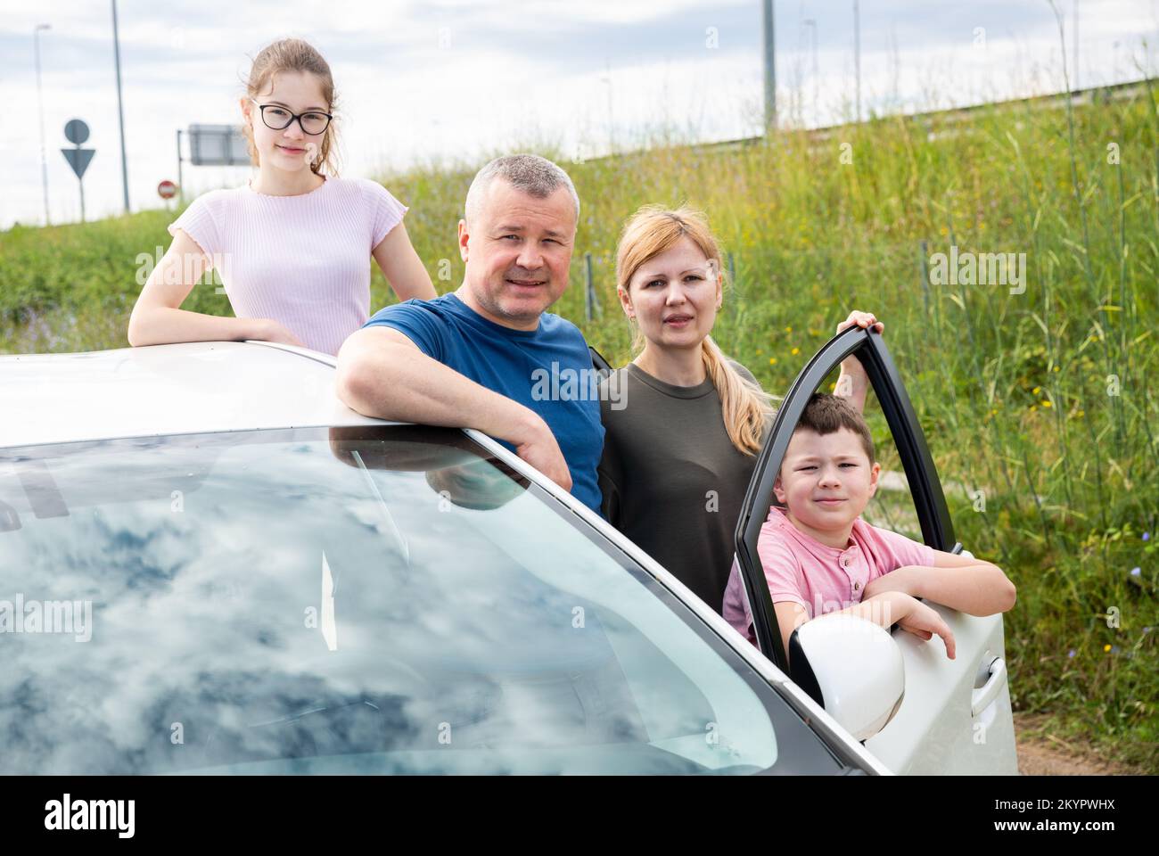 Une famille heureuse de quatre personnes se posant à côté de la voiture achetée Banque D'Images