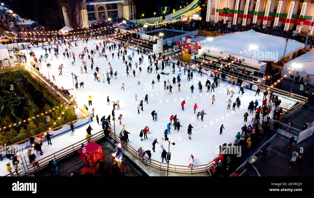 Beau paysage urbain. De nombreuses personnes patinent sur une patinoire en plein air avec illuminations de Noël du nouvel an et guirlandes en soirée d'hiver dans le parc public de la ville. Aerial Drone Voir l'arrière-plan des vacances Banque D'Images