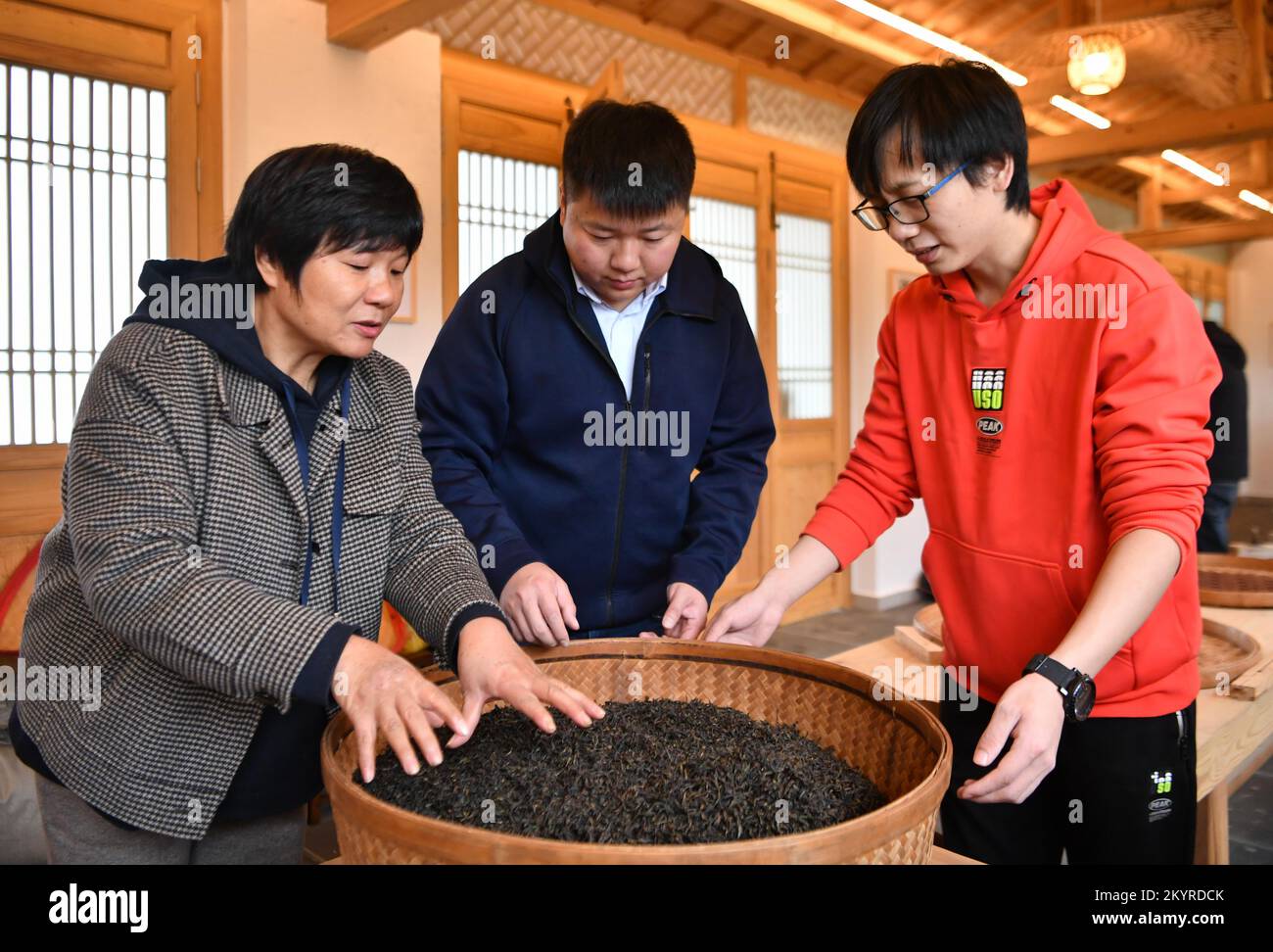 WUYISHAN, 2 décembre 2022 (Xinhua) -- You Yuqiong (L), la seule femme héritante de la technique de fabrication du thé de roche de Wuyi, instruit son fils Fang Zhou (C) dans la technique de torréfaction du thé de roche de Wuyi à Wuyishan, dans la province du Fujian, au sud-est de la Chine, 1 décembre 2022. Wuyishan, la ville natale du thé rock, propose un large éventail de variétés de thé rock. La technique de fabrication du thé de roche Wuyi, une variété spéciale d'oolong avec un goût particulièrement torréfié et un arôme floral et fruité, comprend plus de 10 procédures de transformation, y compris la récolte du thé, le flétrissement, la fixation, la torsion, le séchage et ainsi de suite. Inher Banque D'Images