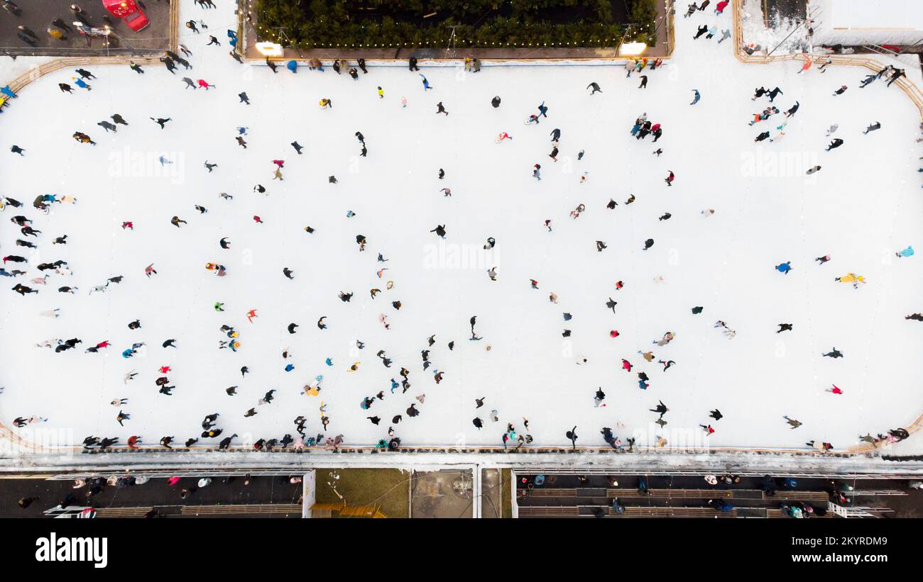 Vue de dessus des personnes qui patinent sur la grande patinoire en plein air le jour de l'hiver. Vol avec vue aérienne sur la foule de personnes qui patinent sur la glace à la patinoire. Sports d'hiver. Fond de patinage. Patinoire municipale. Banque D'Images