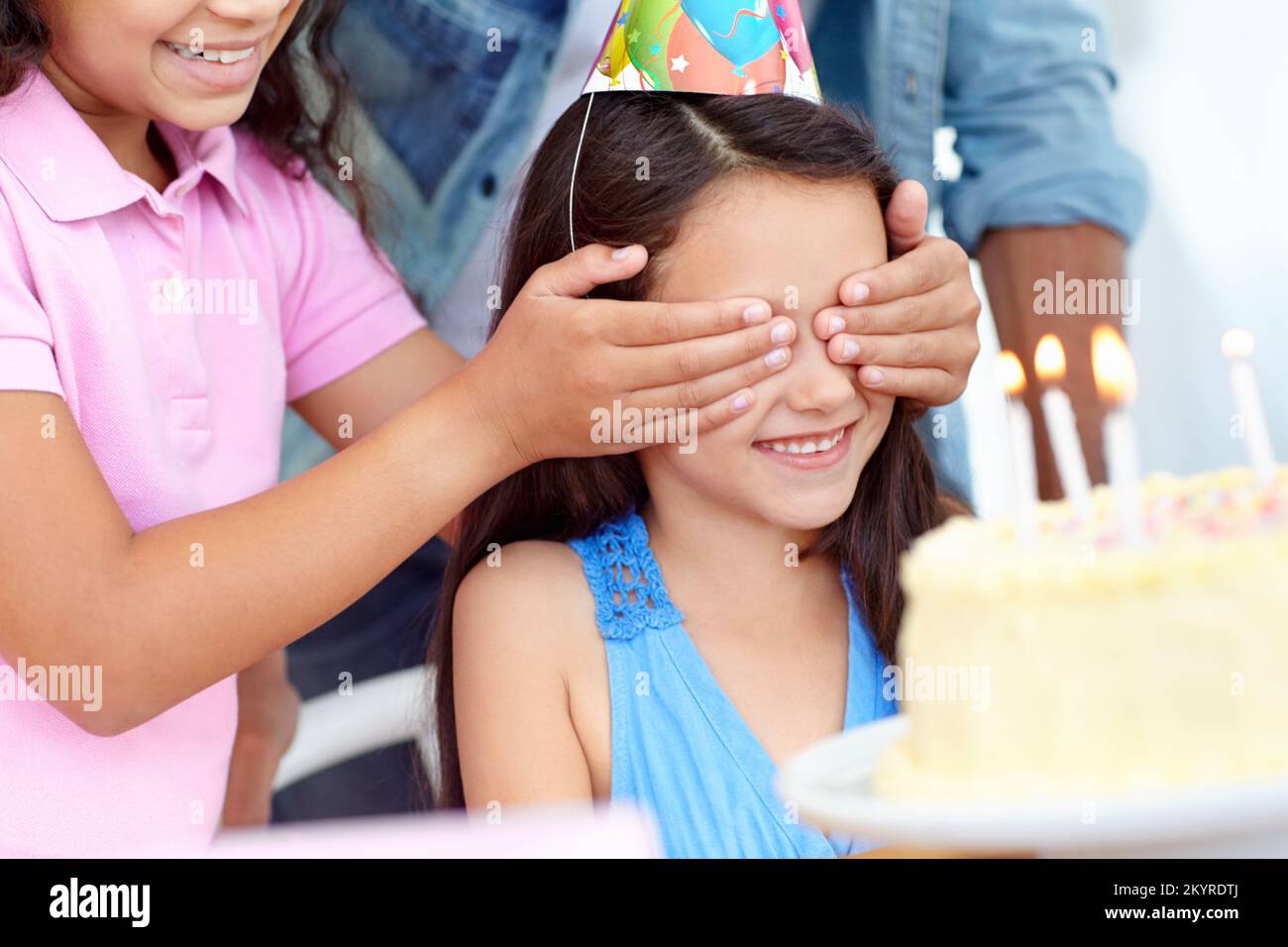 Faites un vœu. une jeune fille couvrant les yeux de ses amis lors d'une fête d'anniversaire. Banque D'Images