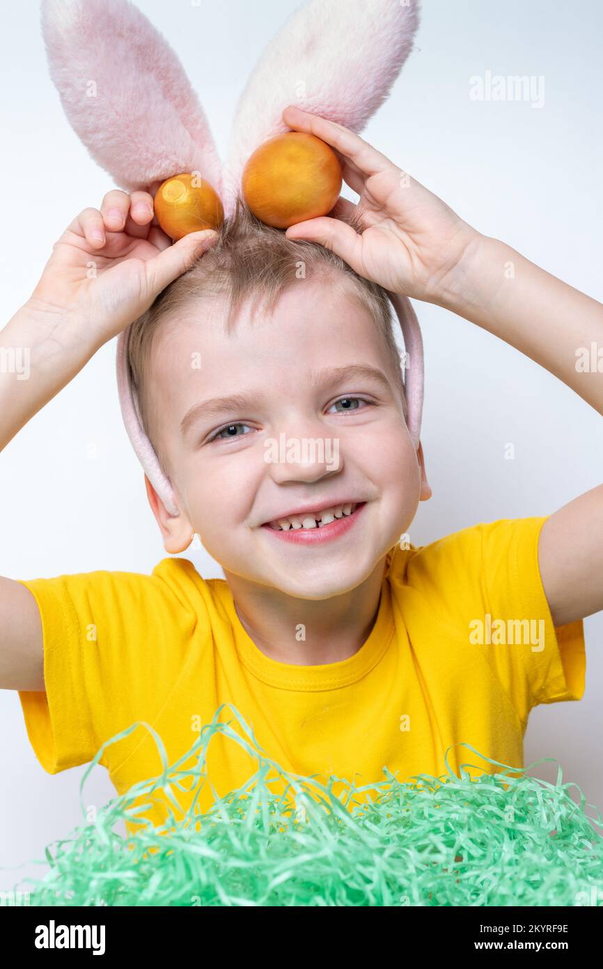 Les enfants célèbrent Pâques. Un enfant drôle dans les oreilles de lapin est à la recherche d'oeufs de Pâques dans le papier vert imitant l'herbe. L'enfant a du plaisir à chasser pour Easte Banque D'Images