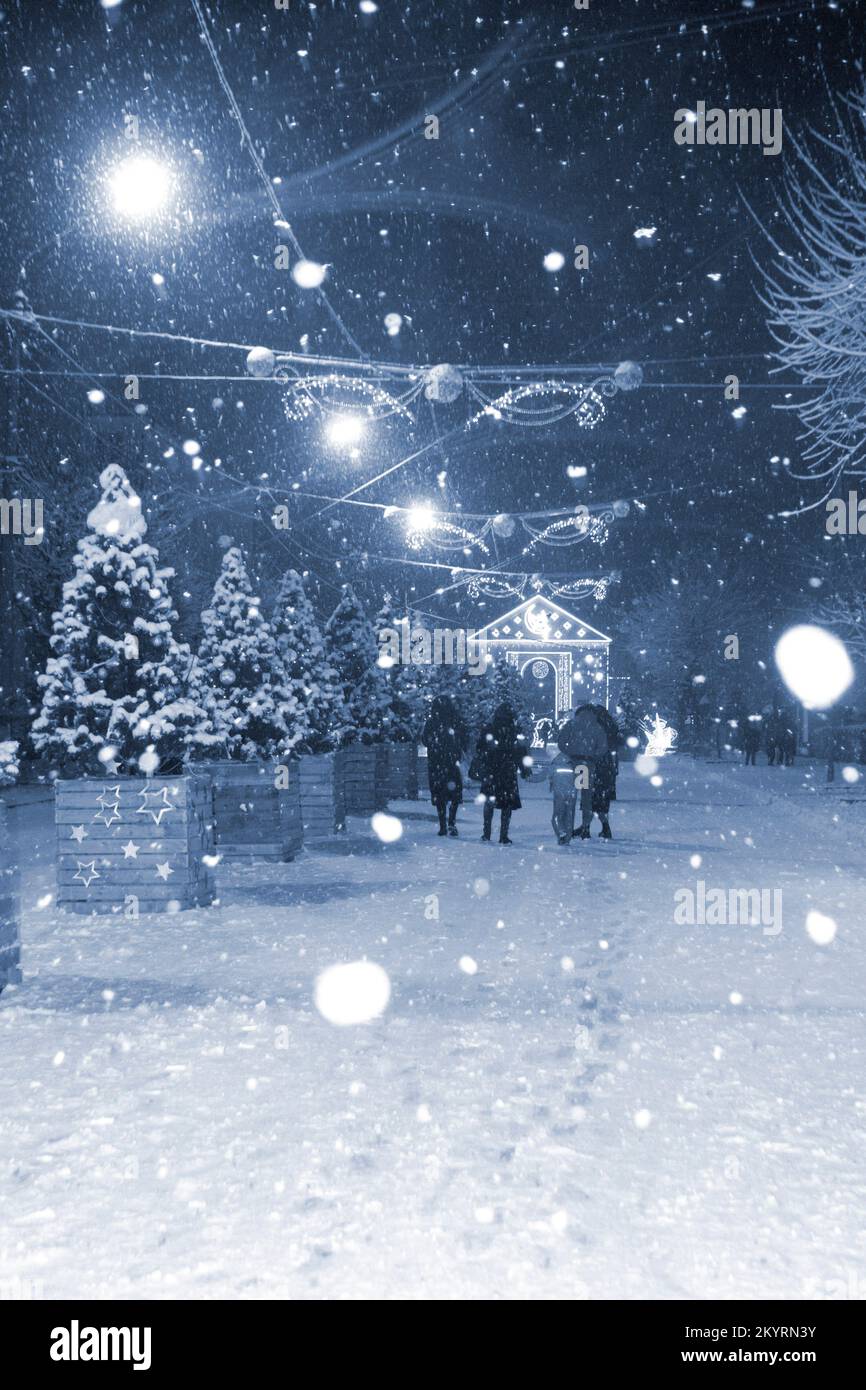 Rue de la ville pendant les fortes chutes de neige pendant la nuit d'hiver. Éclairage décoration lanternes guirlande sur l'arbre de Noël. Couleur bleue Noël fête du nouvel an fond de célébration. taches blanches de flocons de neige Banque D'Images