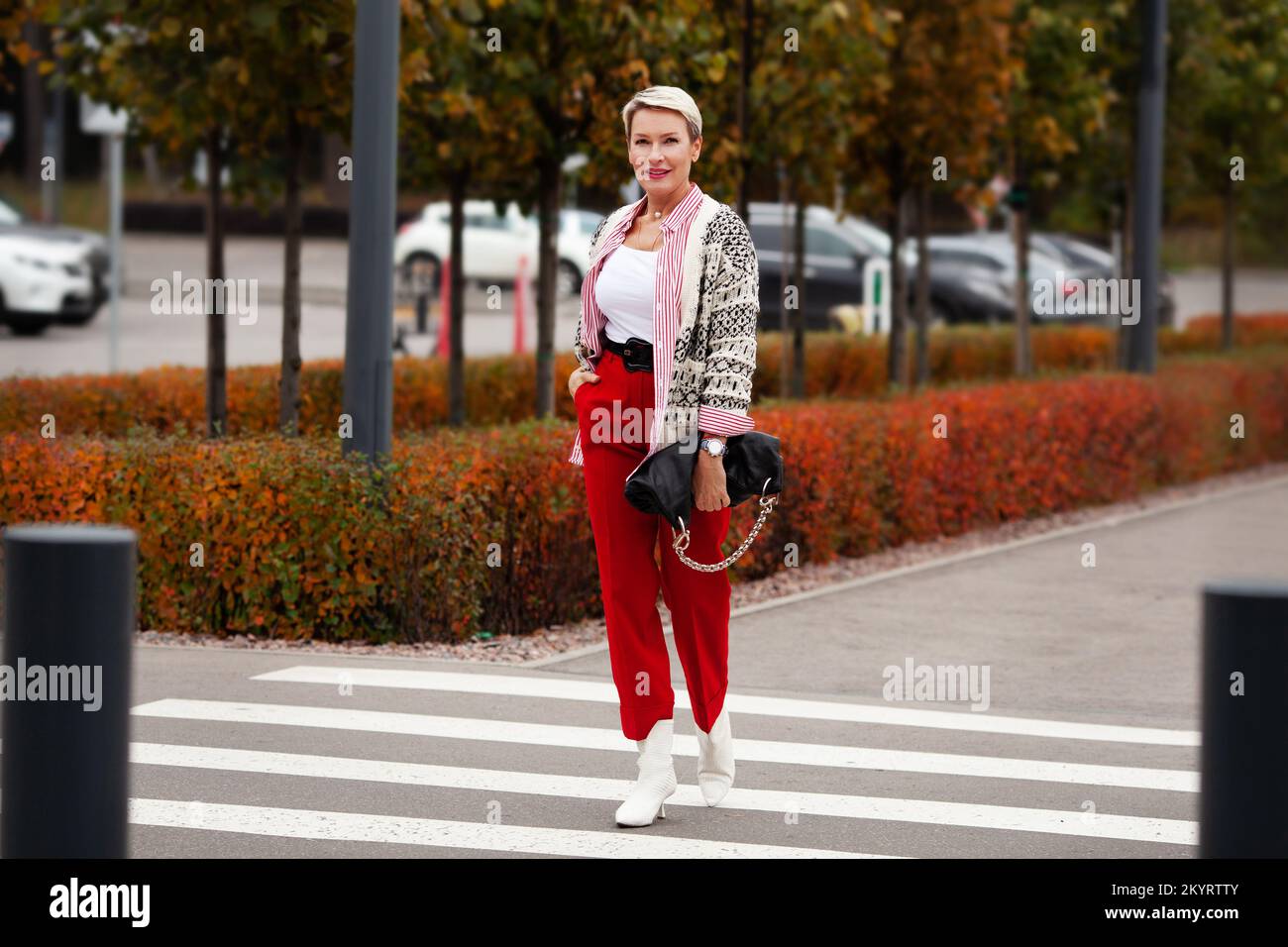 Tendance de la mode pour l'automne. Femme avec une coupe courte qui marche  de l'autre côté de la rue, portant un pantalon rouge, une chemise à rayures,  un gilet tricoté, des chaussures