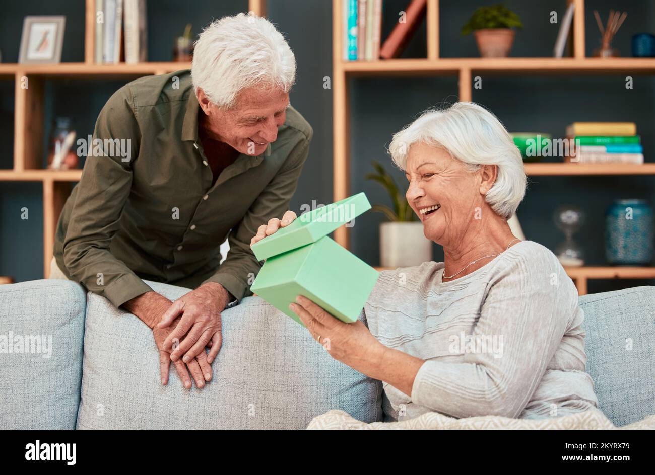 Couple senior, anniversaire et cadeau dans le salon de la maison avec surprise, wow ou amour sur le canapé ensemble. Bonheur, soins ou femme âgée à la retraite, boîte et Banque D'Images