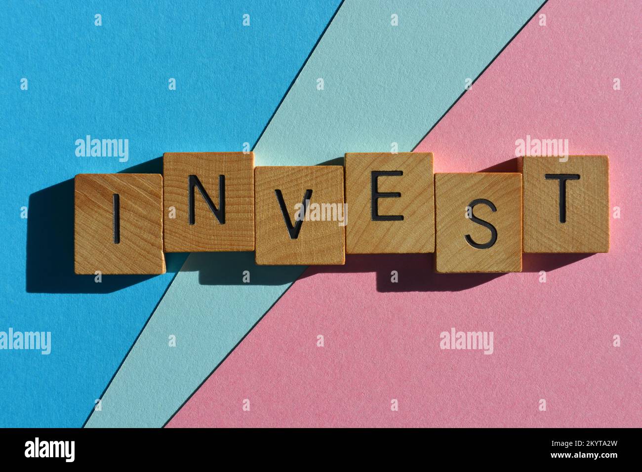 Investir, mot en lettres de l'alphabet en bois isolées sur fond rose et bleu Banque D'Images