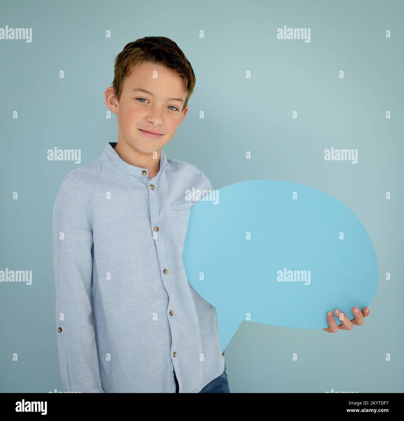 jeune garçon avec chemise bleue et jeans se tient devant le fond bleu et tient la bulle de la parole bleue dans ses mains Banque D'Images