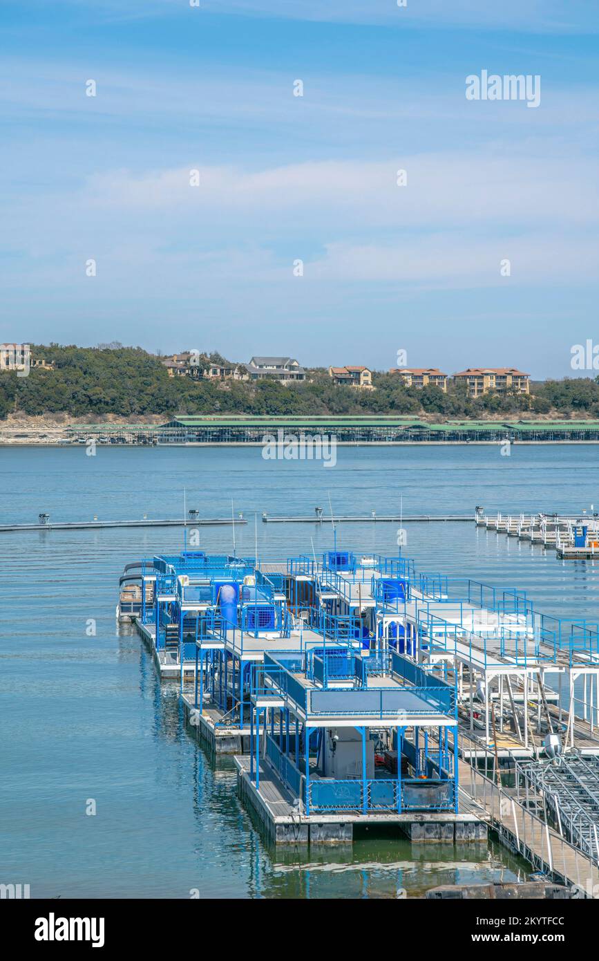 Bateaux de fête plats sur un quai à Lake Austin, Austin, Texas. Il y a une vue sur les grands bâtiments résidentiels en haut de la pente à travers le lac. Banque D'Images