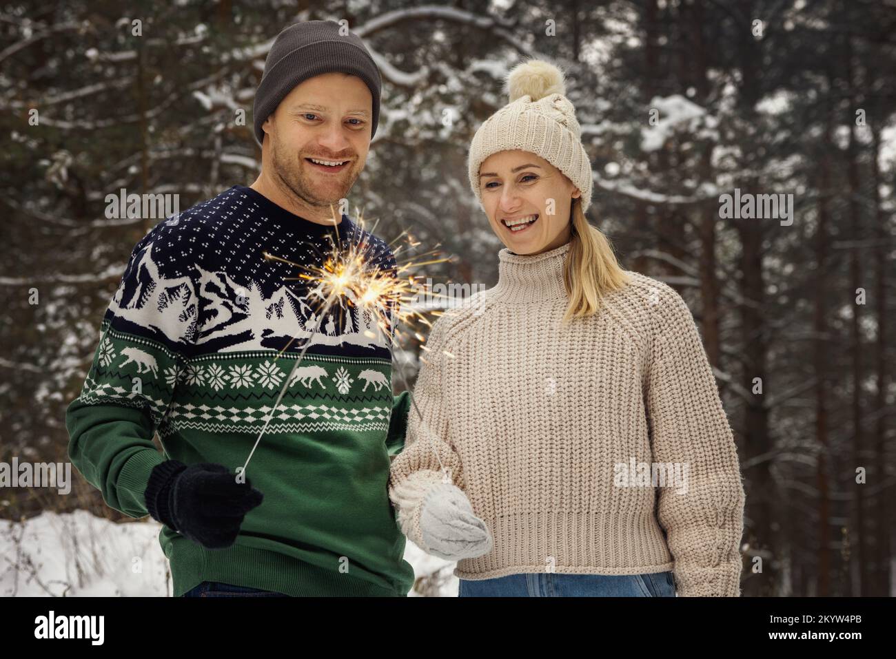 couple souriant avec des spameurs en plein air dans une forêt enneigée d'hiver. personnes avec des lumières du bengale brûlantes Banque D'Images