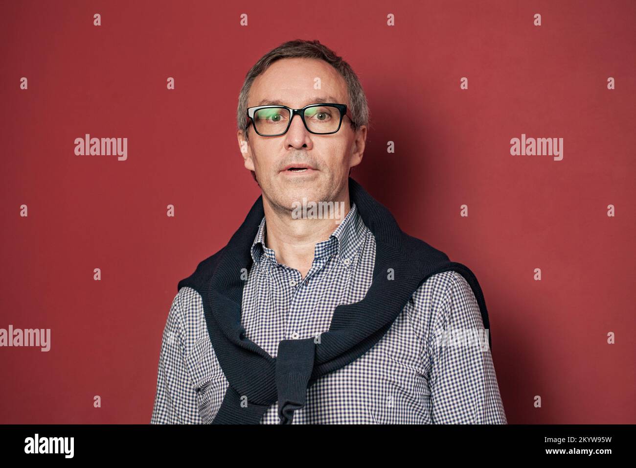 Portrait d'homme d'affaires sérieux et mûr à cheveux gris en chemise et lunettes sur fond rouge Banque D'Images