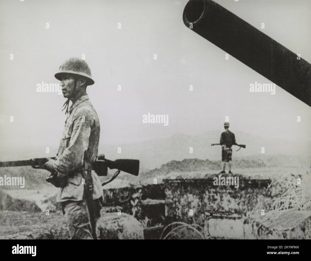 Photo vintage vers 1942 de soldats japonais debout sur la garde avec des fusils à proximité d'un placement d'artillerie côtière pendant la deuxième Guerre mondiale Banque D'Images