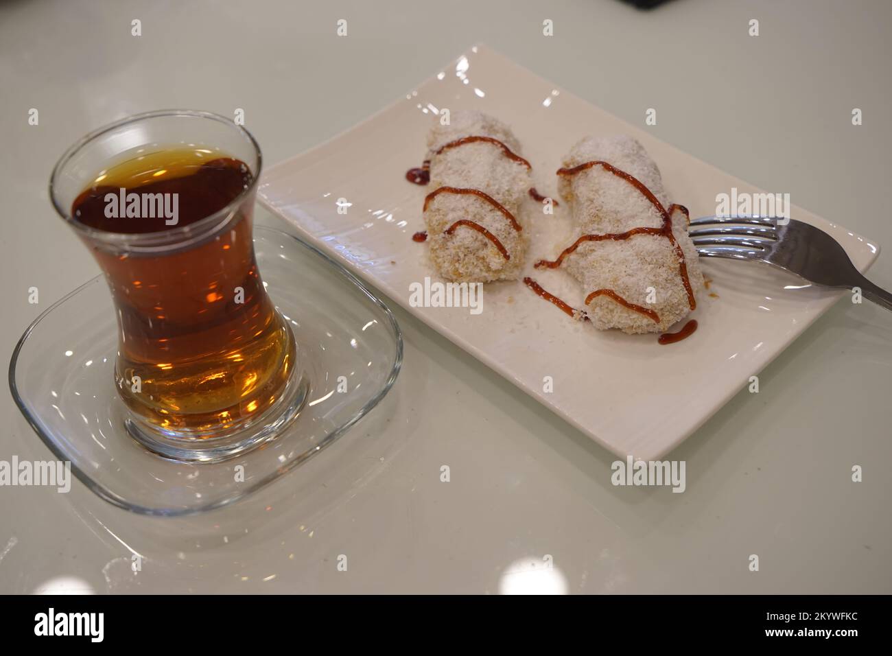 Déjeuner sucré avec gâteau, gelée de fruits et thé dans un verre sur une table blanche, cuillères à café Banque D'Images