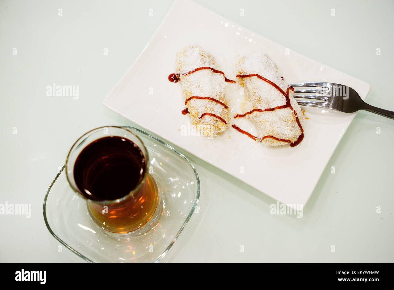 Déjeuner sucré avec gâteau, gelée de fruits et thé dans un verre sur une table blanche, cuillères à café Banque D'Images
