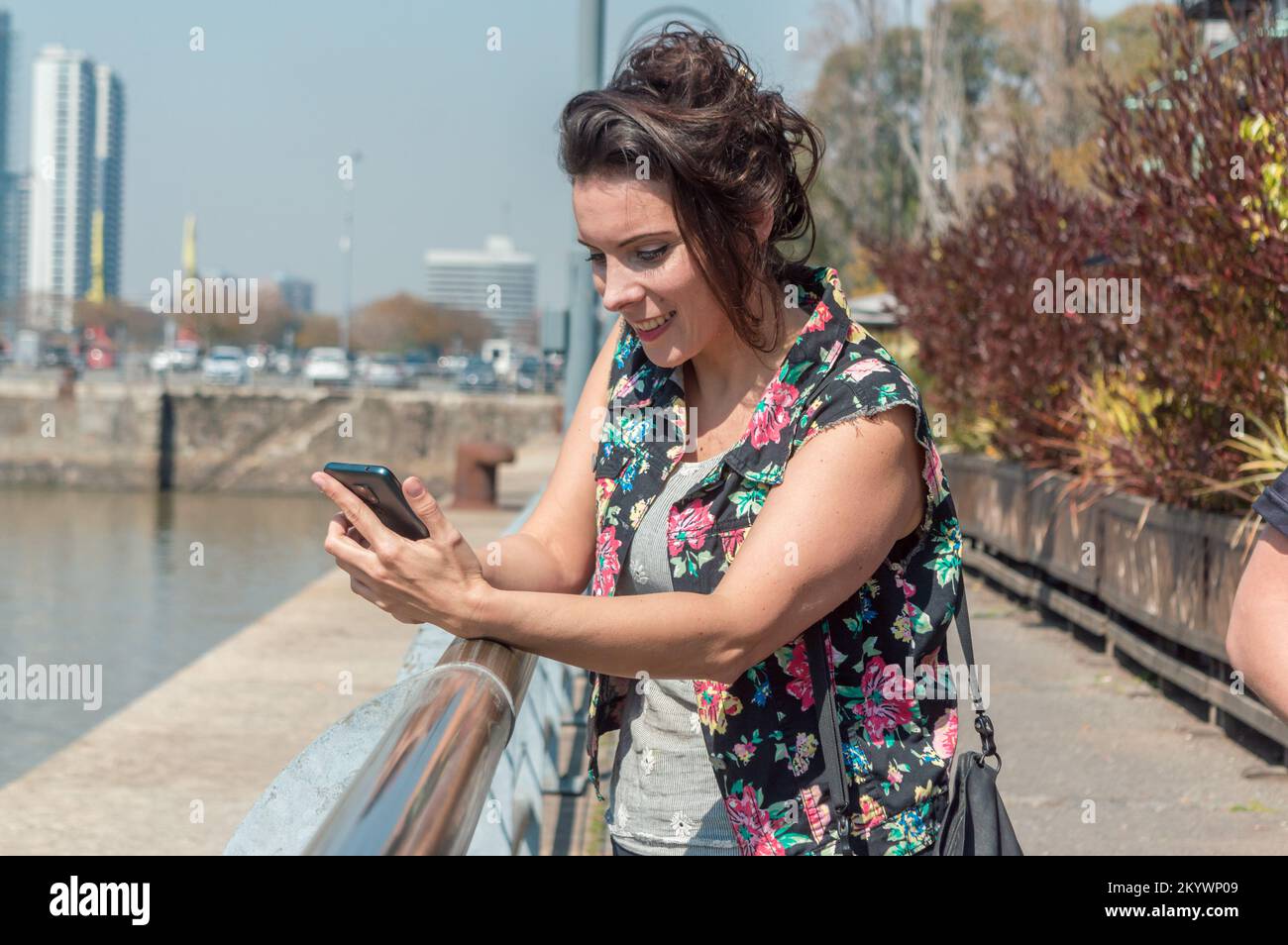 Une femme d'âge caucasien, marchant dans la ville, s'appuie sur une rampe sur ses bras pour vérifier la carte sur son téléphone portable. Banque D'Images