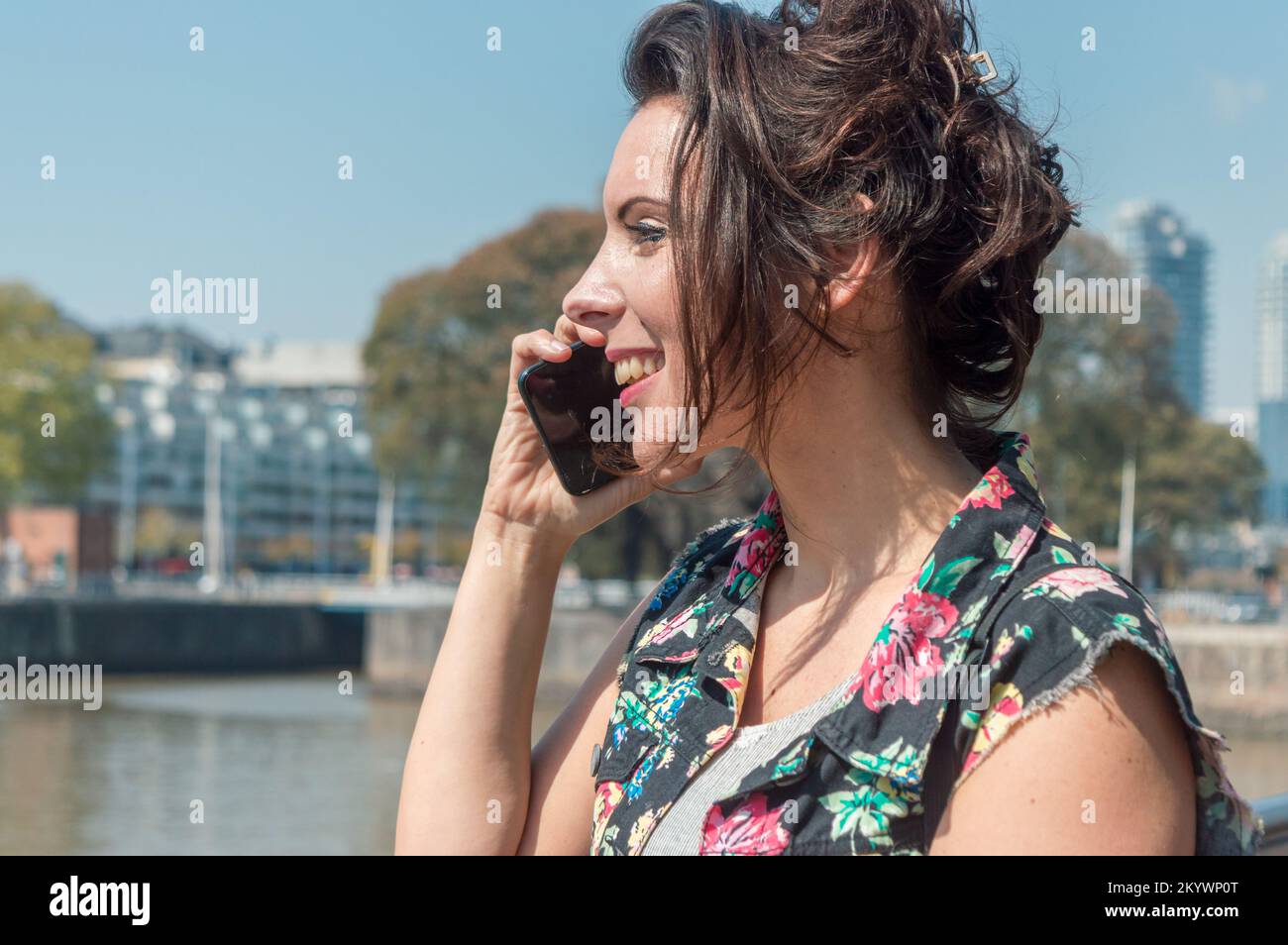 Vue du profil de la bonne femme adulte caucasienne française lors d'un appel téléphonique et souriant dans la rue tout en allant pour une promenade seule. Banque D'Images