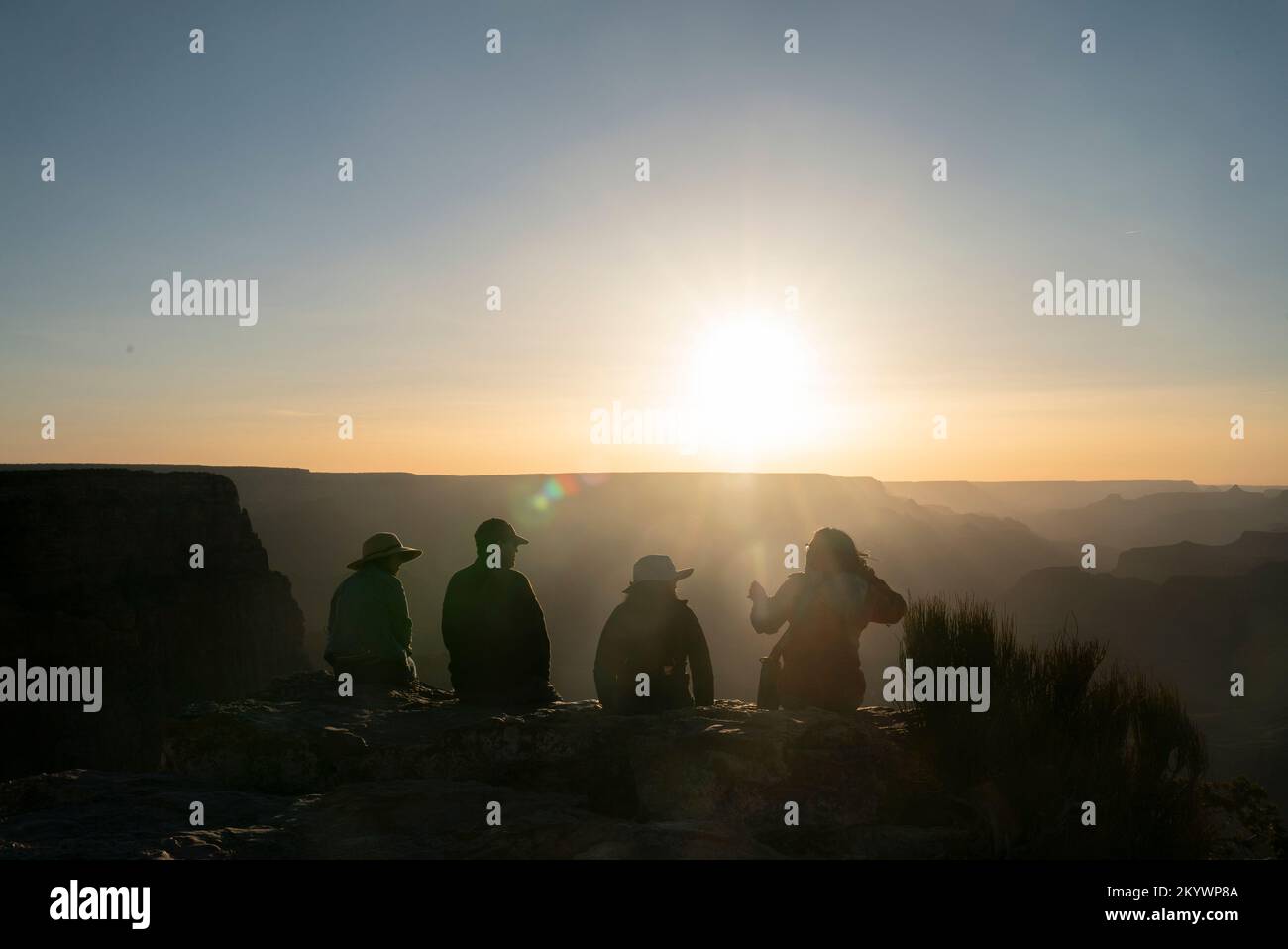 Un groupe de quatre personnes s'assoient sur le rebord du canyon, éclairé par le coucher du soleil Banque D'Images