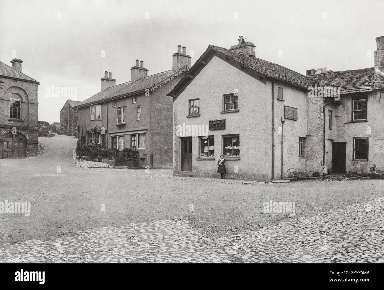 Photographie vintage - 1912 - fille avec poupée à côté de la boutique Mary Noble, Market Square, Hawkshead, Cumbria Banque D'Images