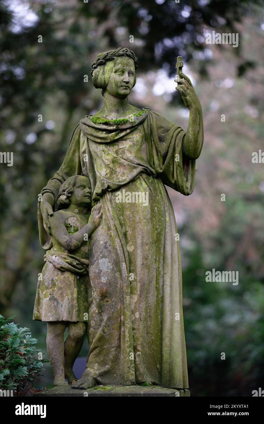une femme historique figure avec un enfant dans un vieux cimetière tenant une petite croix comme un selfie téléphone Banque D'Images