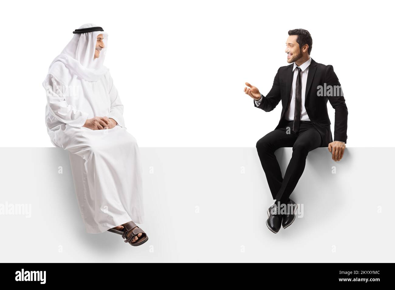 Homme d'affaires et homme arabe dans des clotes ethniques assis sur un panneau blanc ayant une conversation isolée sur fond blanc Banque D'Images
