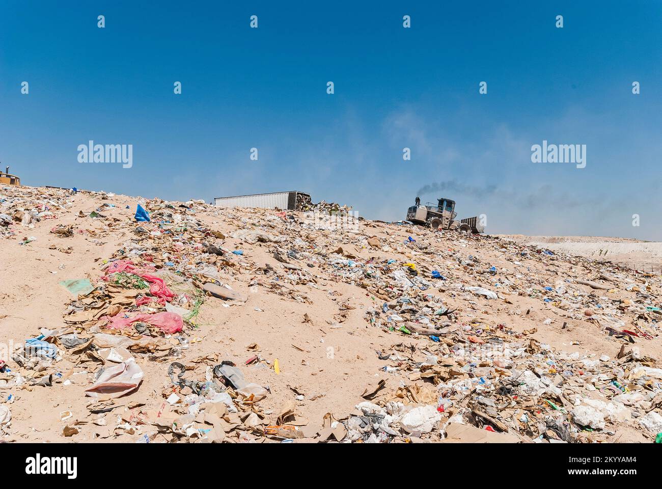 Un compacteur de sol et une semi-remorque sur une pente dans une décharge active. Le compacteur de sol émet de la fumée noire de diesel. Banque D'Images