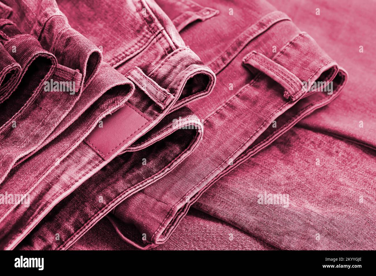 Plusieurs jeans sont empilés dans la salle à manger. Rangée de pantalons Jean denim dans le placard. Concept d'achat, de vente, de shopping et de vêtements modernes à la mode image tons en Viva Magenta, couleur de l'année 2023 Banque D'Images