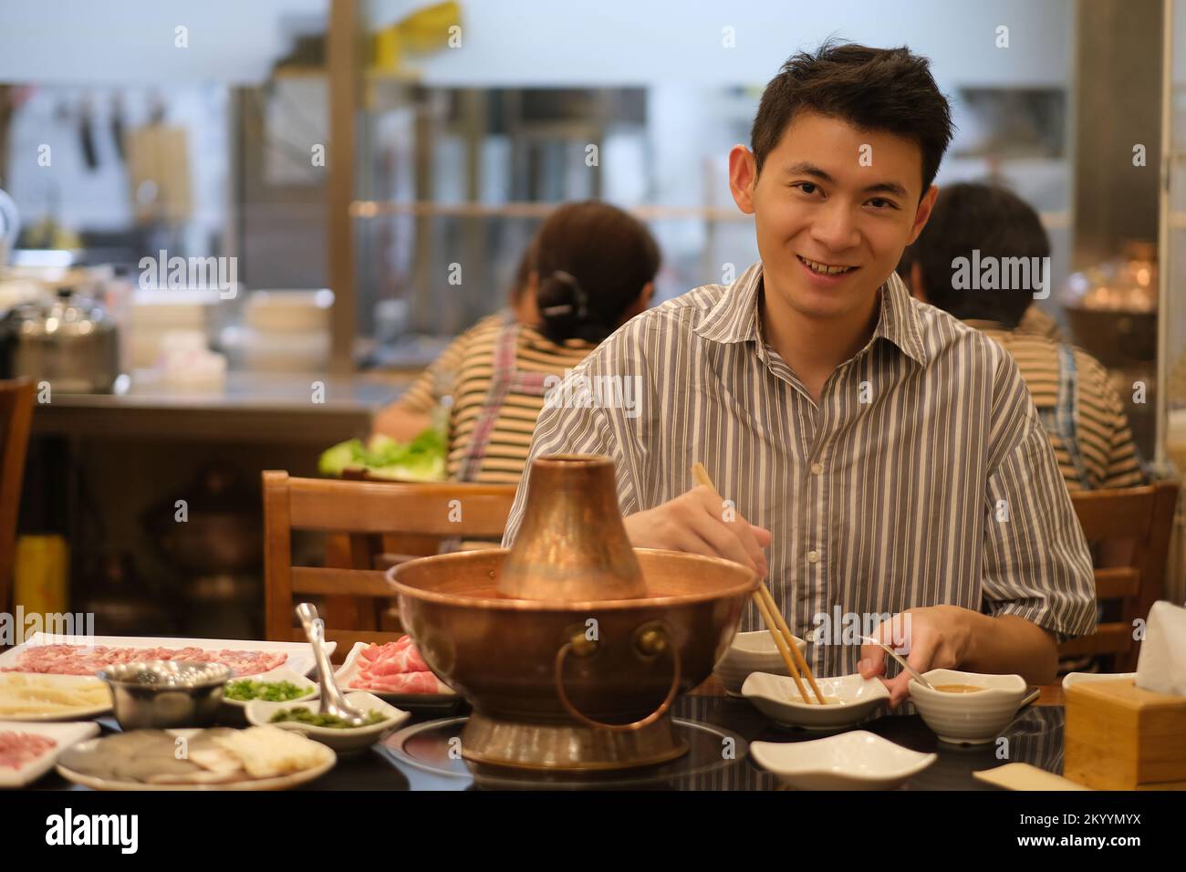 Beau jeune homme asiatique mangeant un hot pot chinois traditionnel dans le restaurant, regardant l'appareil photo Banque D'Images