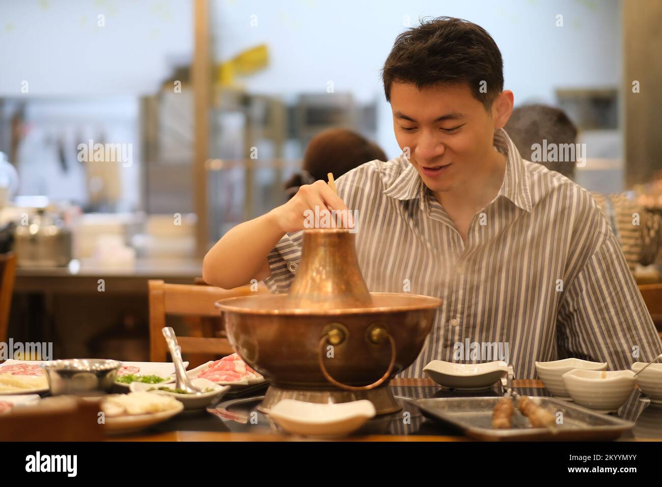 Jeune homme chinois souriant mangeant un hot pot à mouton bouilli instantané dans le restaurant, un hot pot chinois traditionnel Banque D'Images