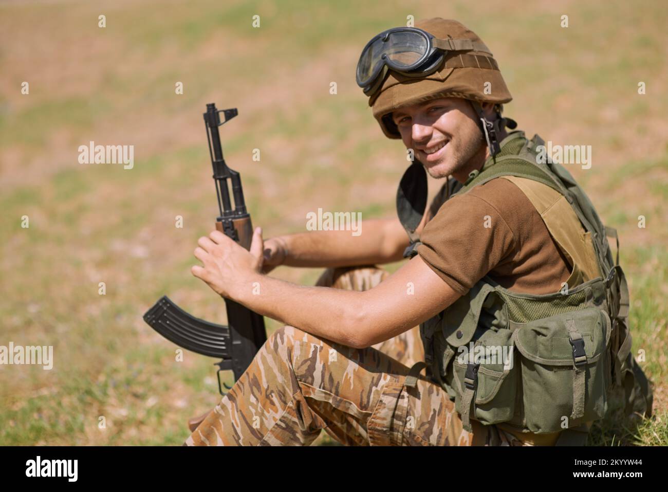 Heureux d'être de service. Un jeune soldat assis sur l'herbe à l'extérieur. Banque D'Images