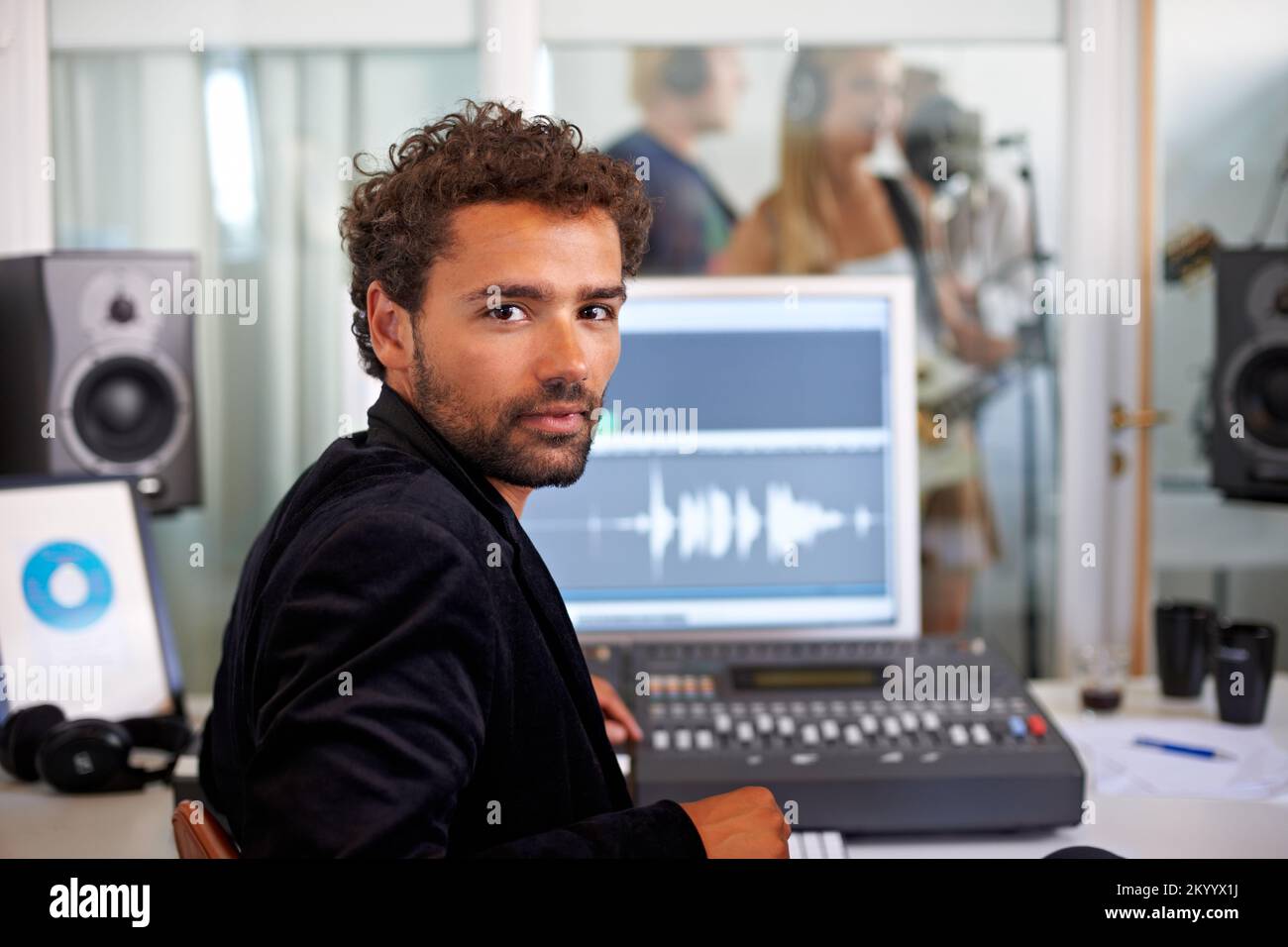 Transformer les talents en graphiques. Un jeune ingénieur audio regardant par-dessus son épaule avec son bureau de mixage et une bande en arrière-plan. Banque D'Images