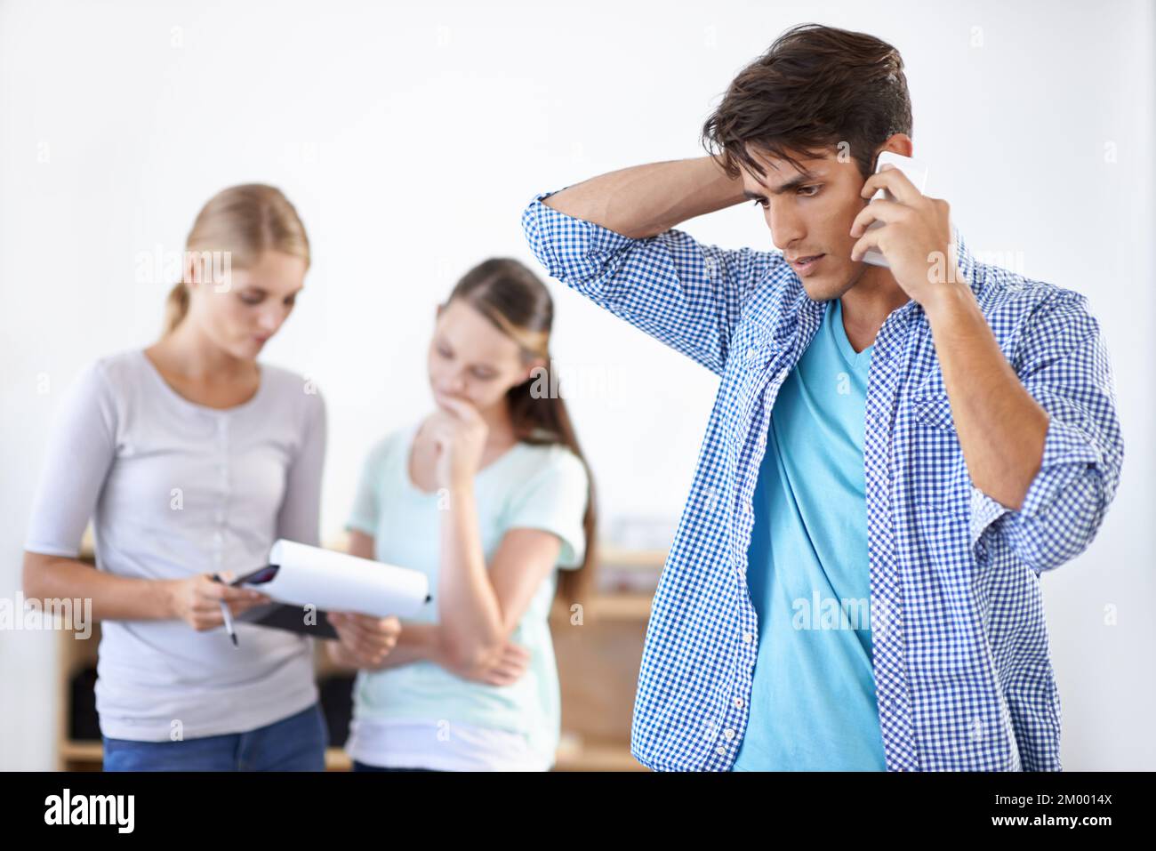 Tirer le meilleur parti d'une réclamation client. Un jeune homme parlant au téléphone avec ses collègues debout à l'arrière-plan. Banque D'Images