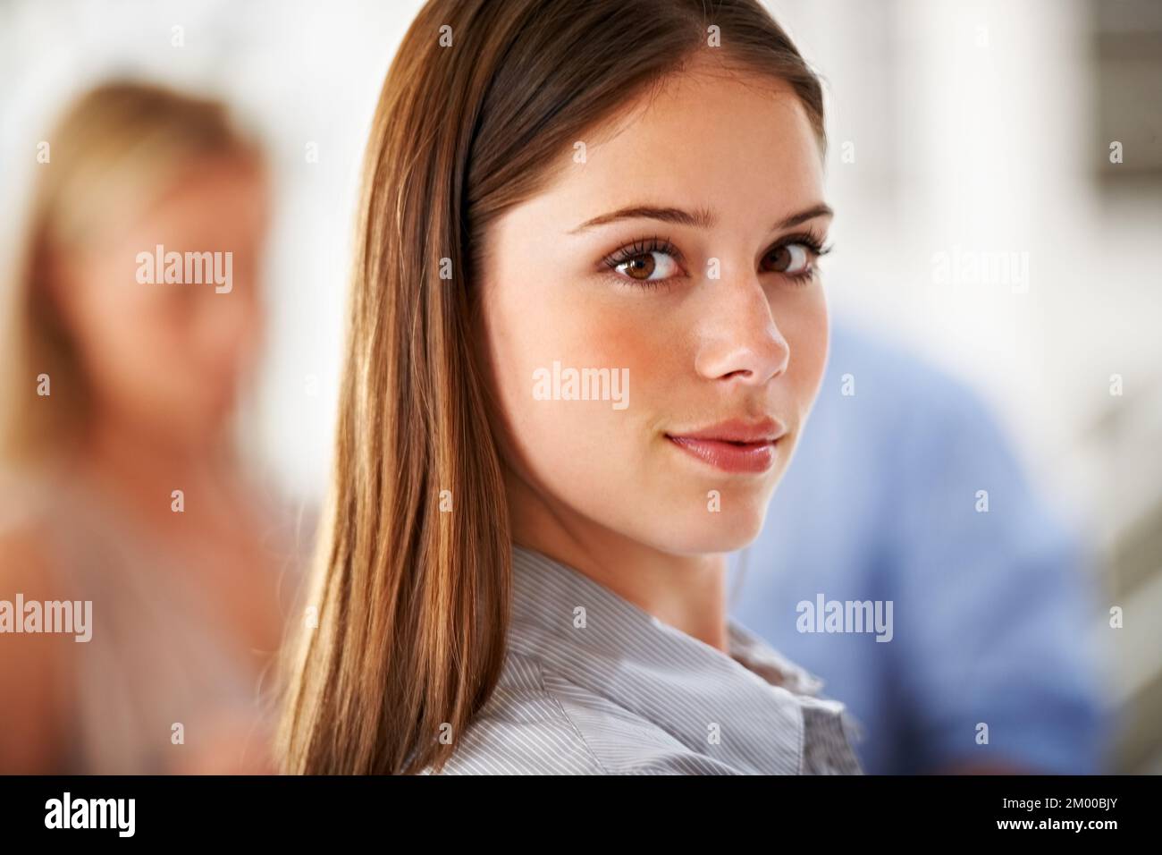 Je prends la tête de mon équipe par messagerie instantanée. Un leader souriant à l'appareil photo avec des collègues flous en arrière-plan. Banque D'Images