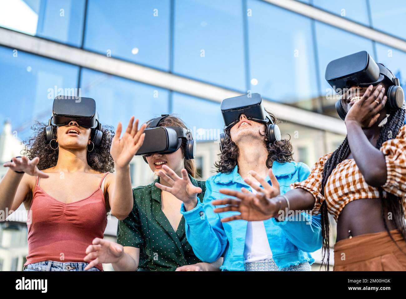 Quatre jeunes femmes qui essaient la réalité virtuelle avec des micro-casques modernes, un groupe de personnes jouant avec des lunettes de protection dans l'AR, un monde virtuel et de nouvelles technologies pour le divertissement Banque D'Images